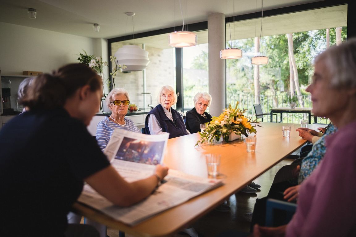 Frauen und Männer sitzen am Tisch Pfleger liest Tageszeitung vor im Pflegeheim in Hannover Landhaus Pflege und Wohnen